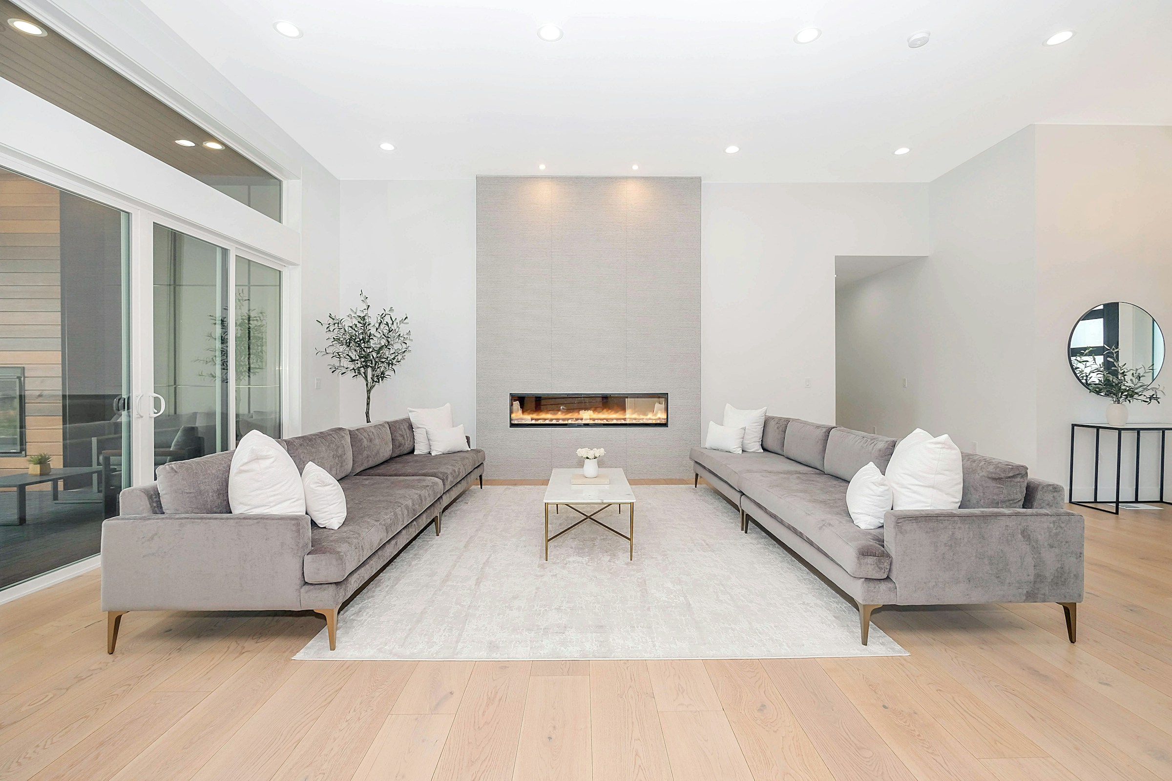 Ein modernes Wohnzimmer, hellgraue Töne, beidseits ein bequemes Sofa, mittig ein Wandkamin